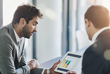 Två män i kostym pratar kring en skärm med ekonomiska data på